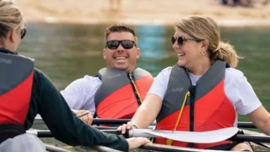 Group of three people kayaking with clear canoes, wearing life vests and smiling.