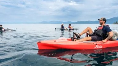 People kayaking on a calm lake under a cloudy sky.