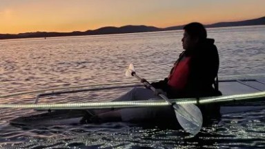 Person kayaking on a calm lake at sunset with mountains in the background.