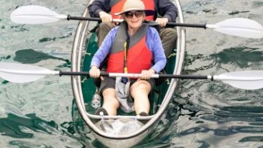 Two people kayaking on calm water, wearing hats and red life vests.